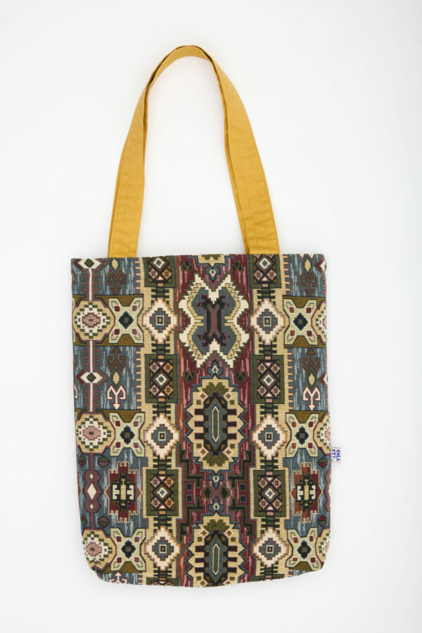 Voyagez entre tradition et modernité avec ce totebag 38 × 58 × 8 cm. Sa première face déploie un jacquard inspiré des kilims, mêlant ocre, bordeaux, vert sauge et touches indigo ; la seconde, plus épurée, joue sur un motif feuillu sable ton‑sur‑ton encadré de kaki. Les anses miel illuminent l’ensemble. Confectionné à partir de textiles recyclés et cousu à la main, chaque sac raconte l’engagement durable de Chkarty et la finesse de l’artisanat tunisien. 📏 38 × 58 × 8 cm 👜 Double face : jacquard kilim multicolore & motif feuillage graphique sable/kaki 🧵 Totebag écoresponsable fait main en Tunisie – chaque pièce est unique