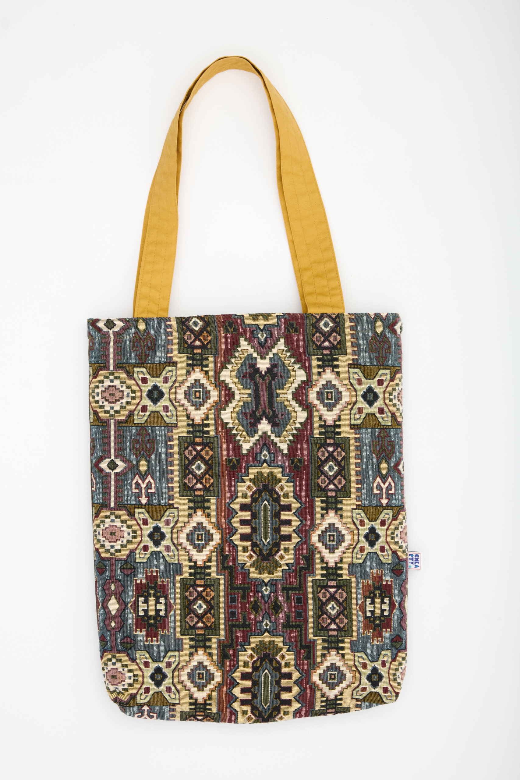 Voyagez entre tradition et modernité avec ce totebag 38 × 58 × 8 cm. Sa première face déploie un jacquard inspiré des kilims, mêlant ocre, bordeaux, vert sauge et touches indigo ; la seconde, plus épurée, joue sur un motif feuillu sable ton‑sur‑ton encadré de kaki. Les anses miel illuminent l’ensemble. Confectionné à partir de textiles recyclés et cousu à la main, chaque sac raconte l’engagement durable de Chkarty et la finesse de l’artisanat tunisien. 📏 38 × 58 × 8 cm 👜 Double face : jacquard kilim multicolore & motif feuillage graphique sable/kaki 🧵 Totebag écoresponsable fait main en Tunisie – chaque pièce est unique